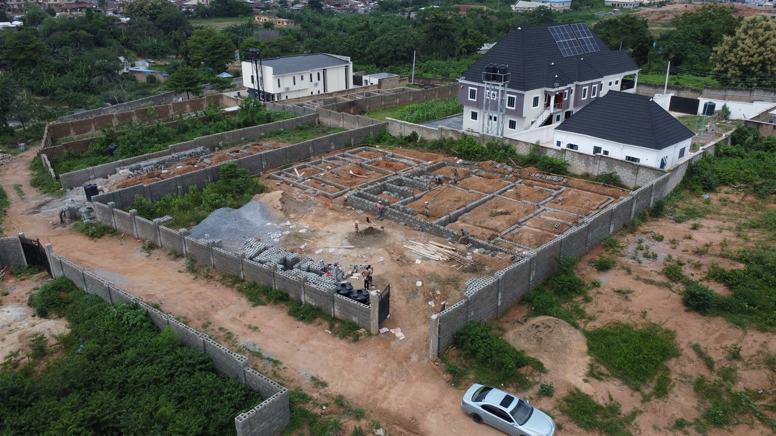 Aerial view of the Eden site at week 3: foundation blockwork laid out for all three homes with materials staged in the compound